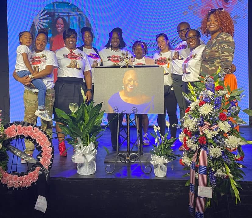Members gathered on stage at a memorial tribute with floral arrangements