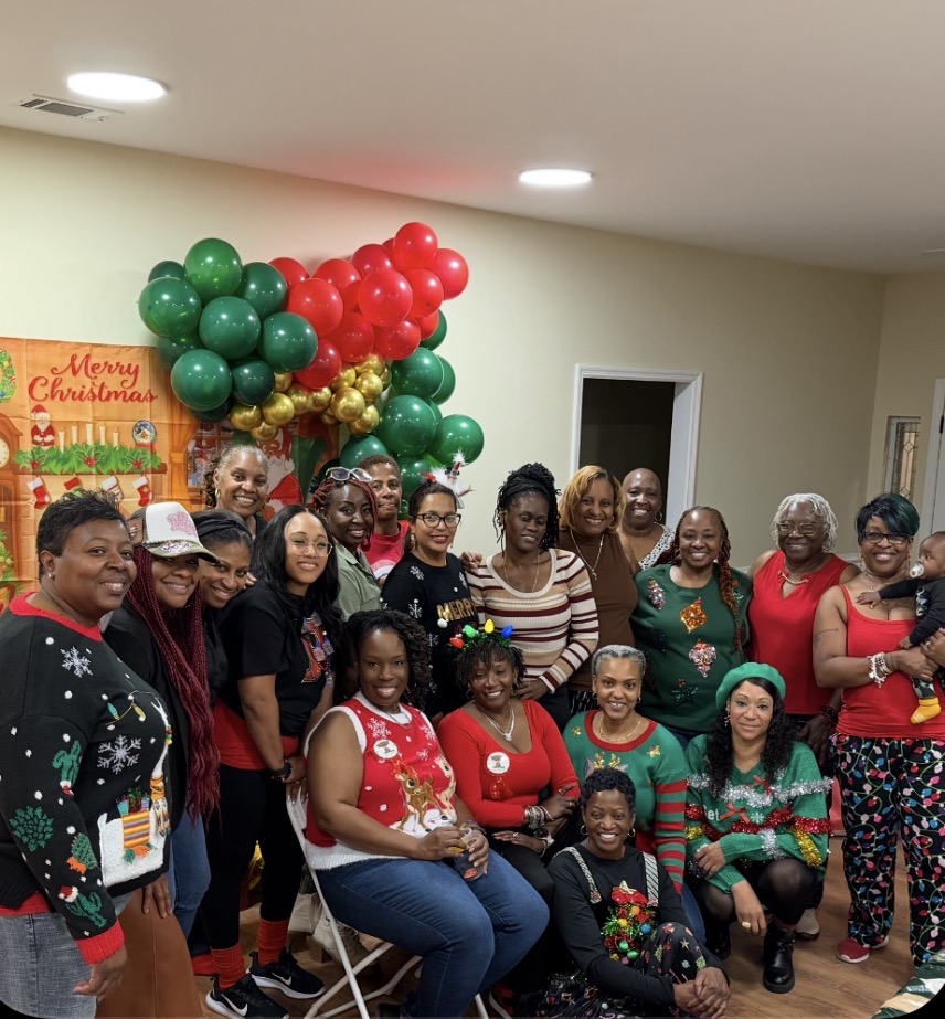 Group photo of members in ugly Christmas sweaters by a balloon arch