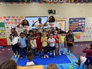 Members visiting an elementary classroom with children saluting